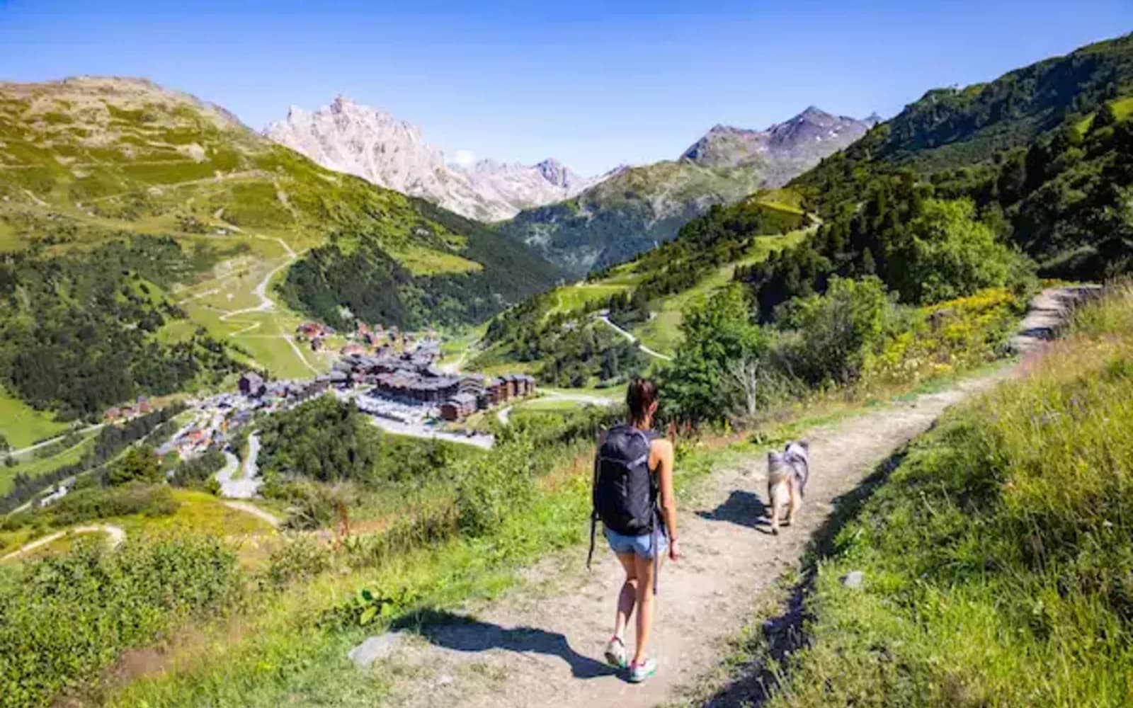 Randonneur sur un sentier fleuri de Méribel en été, avec les sommets des Alpes en arrière-plan